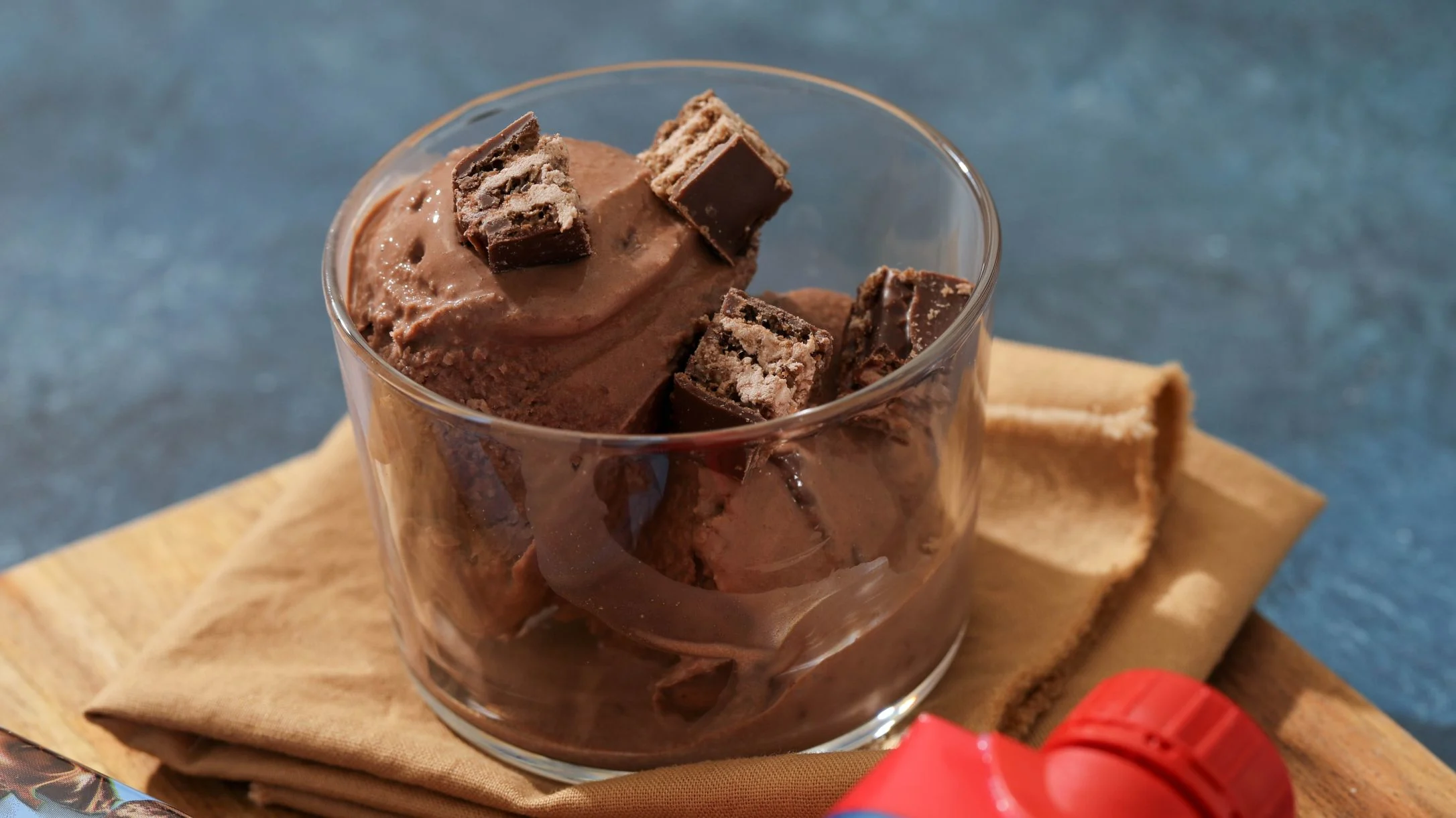 Chocolate ice cream in a glass cup topped with wafer candy pieces, served on brown paper with a blue background.