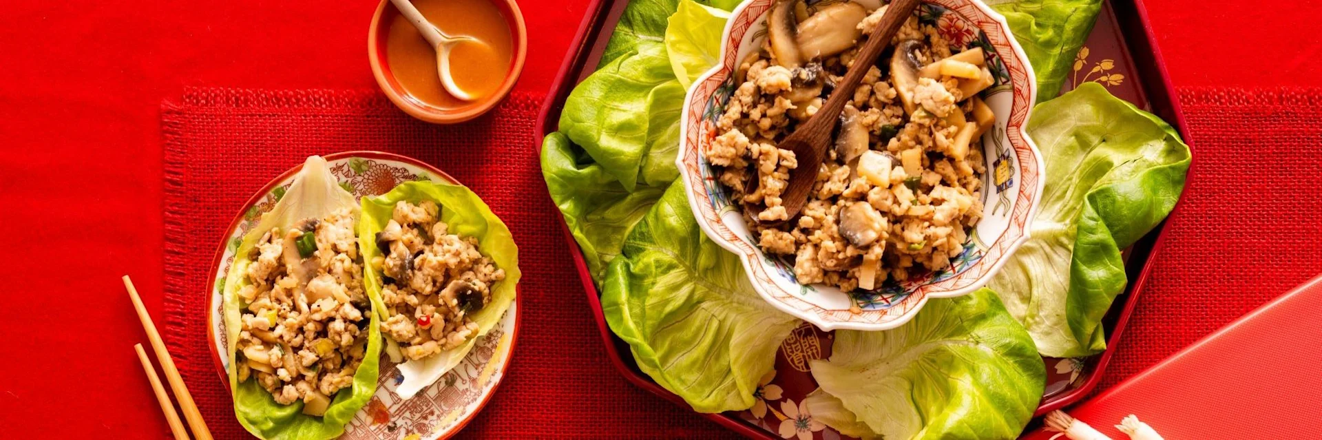 Asian lettuce wraps with ground meat and mushroom filling, served with dipping sauce on a vibrant red background.