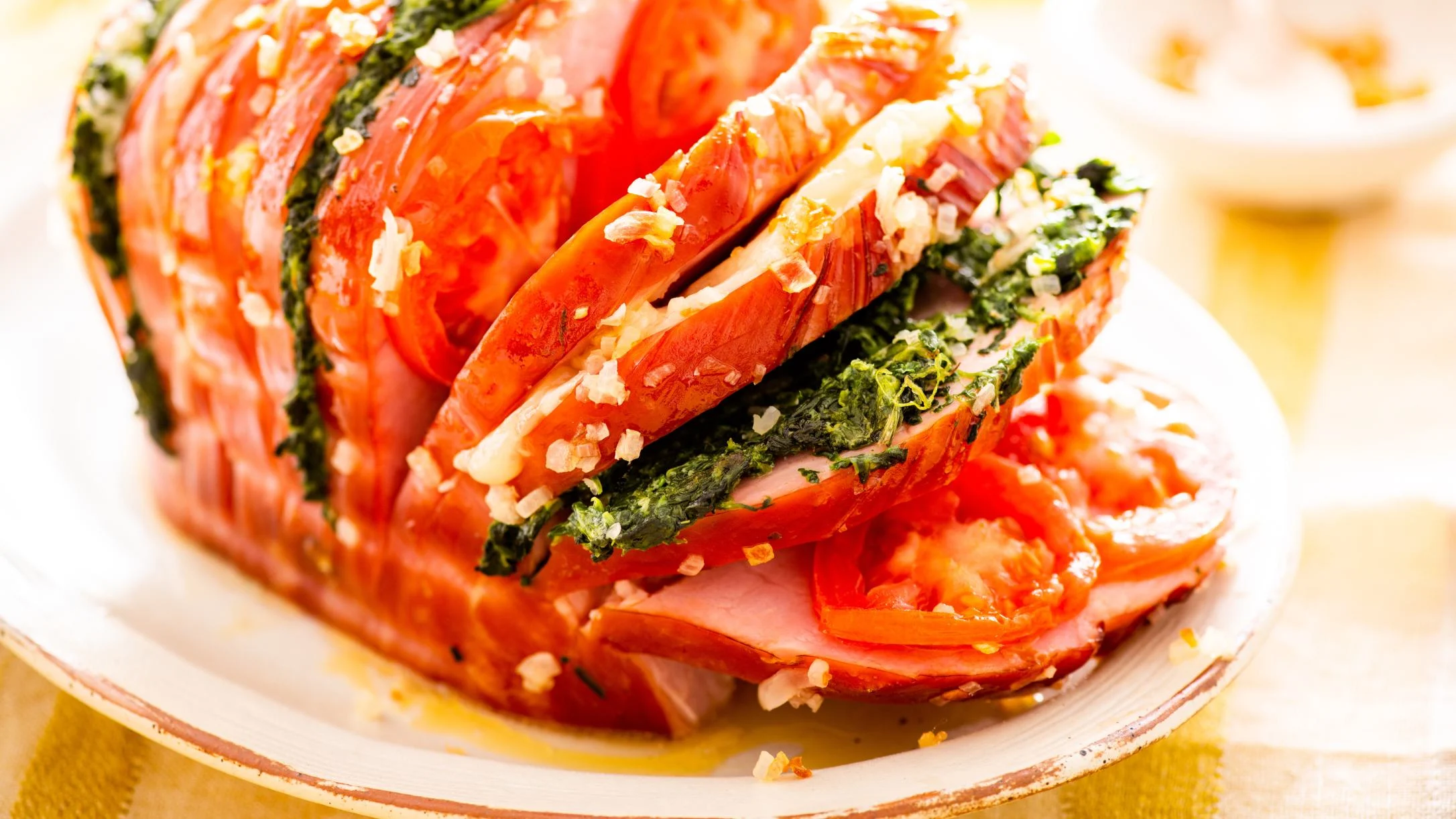 Sliced ham and tomato dish layered with spinach and garlic, served on a white plate with drizzled olive oil.