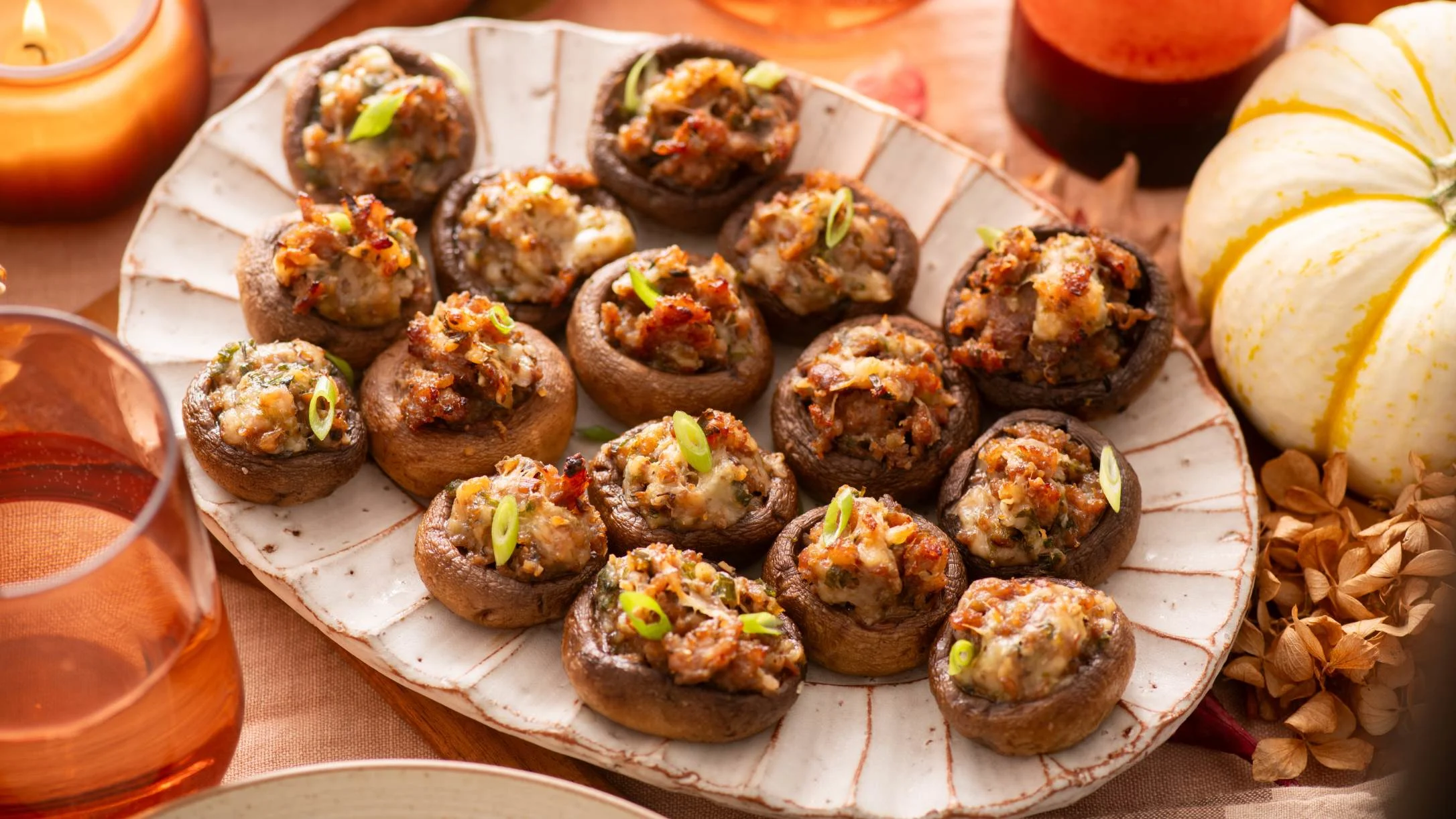Stuffed mushrooms garnished with green onions on a white plate, surrounded by candles and rosé wine in a fall setting.