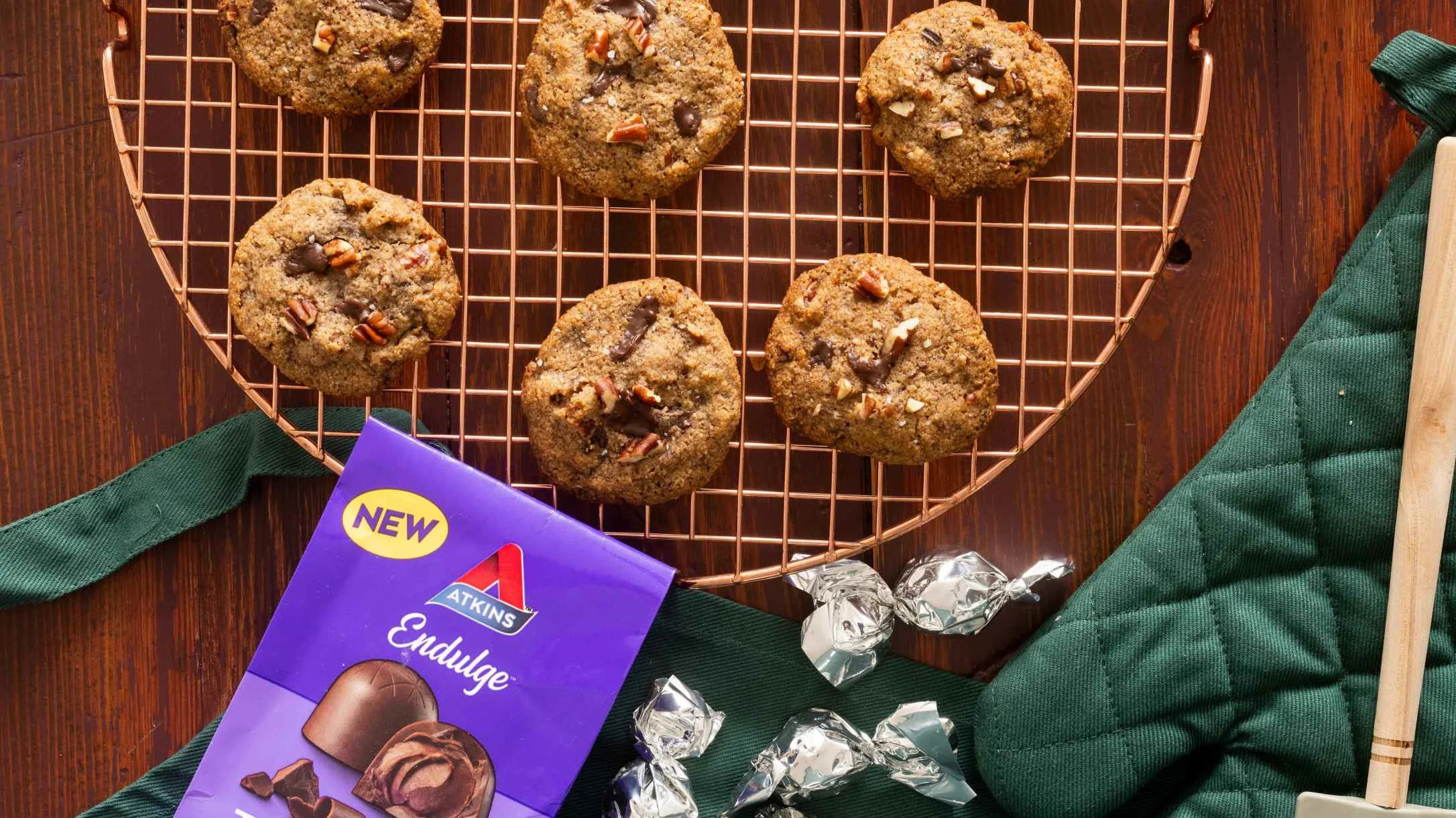 Homemade chocolate pecan cookies on copper cooling rack with Atkins Endulge chocolates and green kitchen towel.