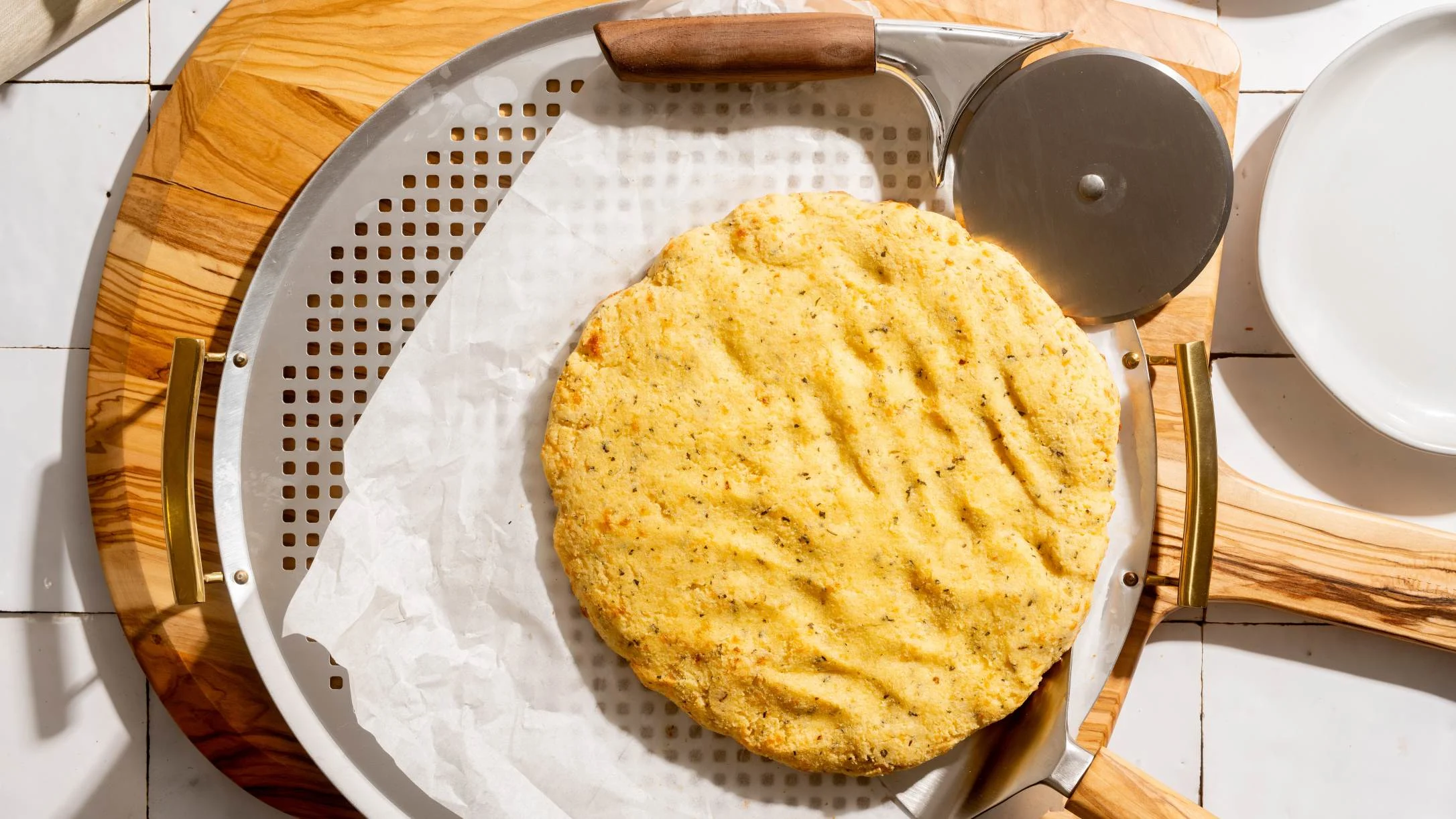 Freshly baked pizza dough on parchment paper in a metal serving tray with wooden handles on a cutting board.