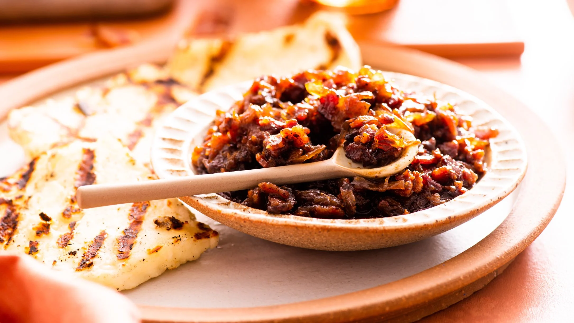 Sweet bacon chutney or relish served in a rustic bowl with a wooden spoon, accompanied by grilled halloumi.