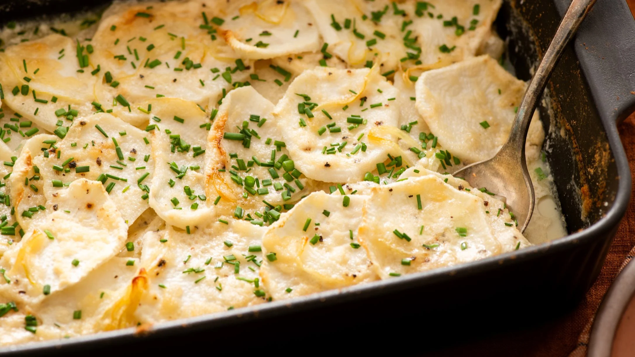 Creamy faux potato gratin in a baking dish with thinly sliced vegetables topped with fresh chopped chives and black pepper.