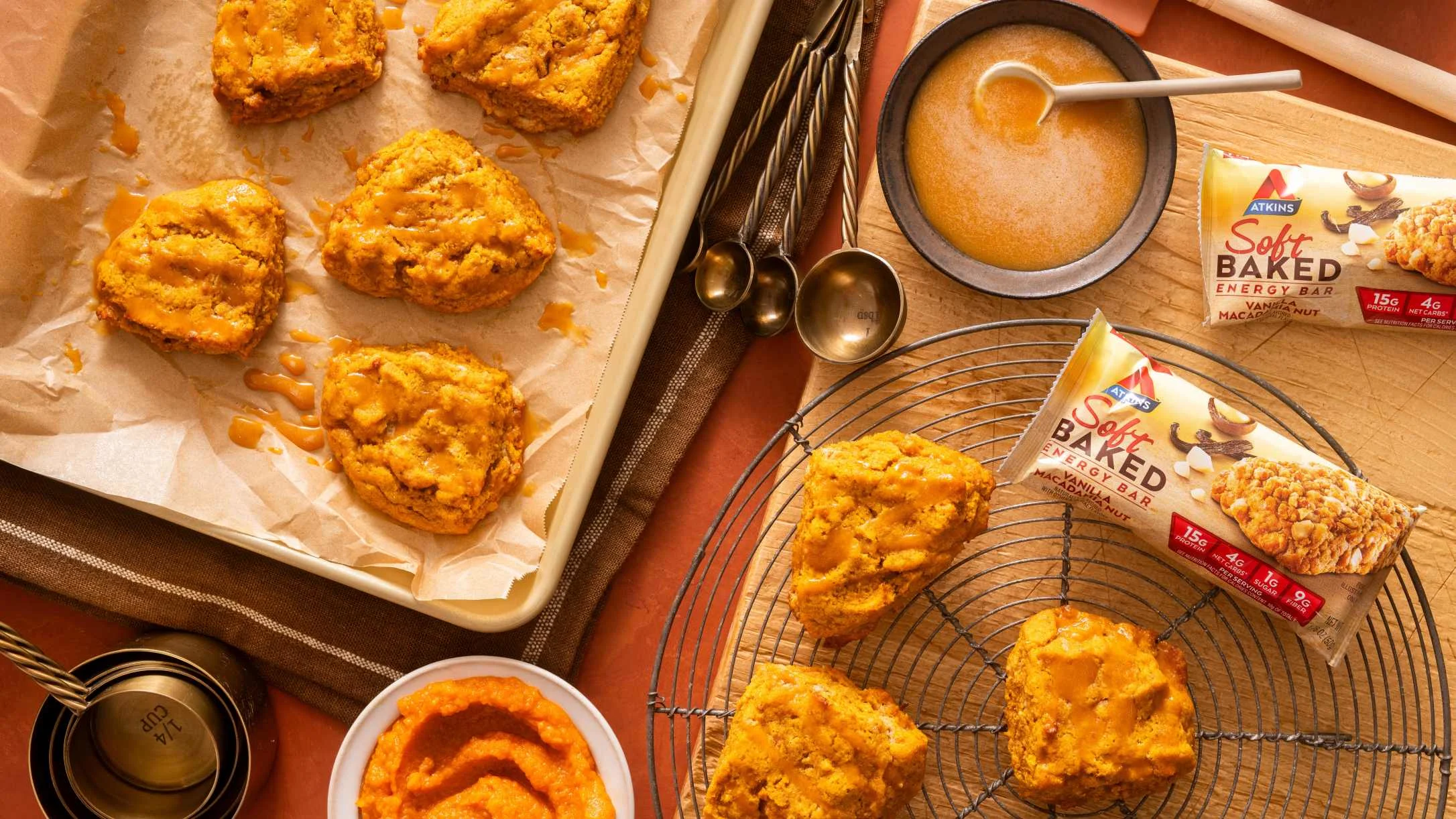 Freshly baked pumpkin scones on baking tray and cooling rack with Atkins energy bars and measuring spoons nearby.