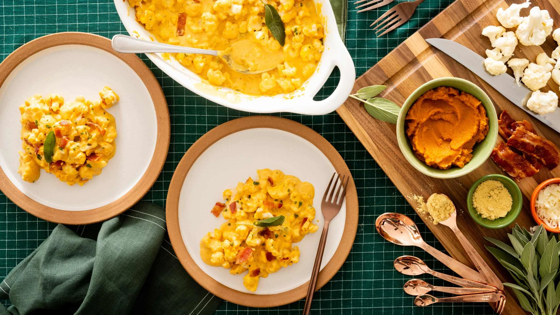 Creamy cauliflower casserole served on plates with pumpkin puree, raw cauliflower, and herbs on a wooden board.