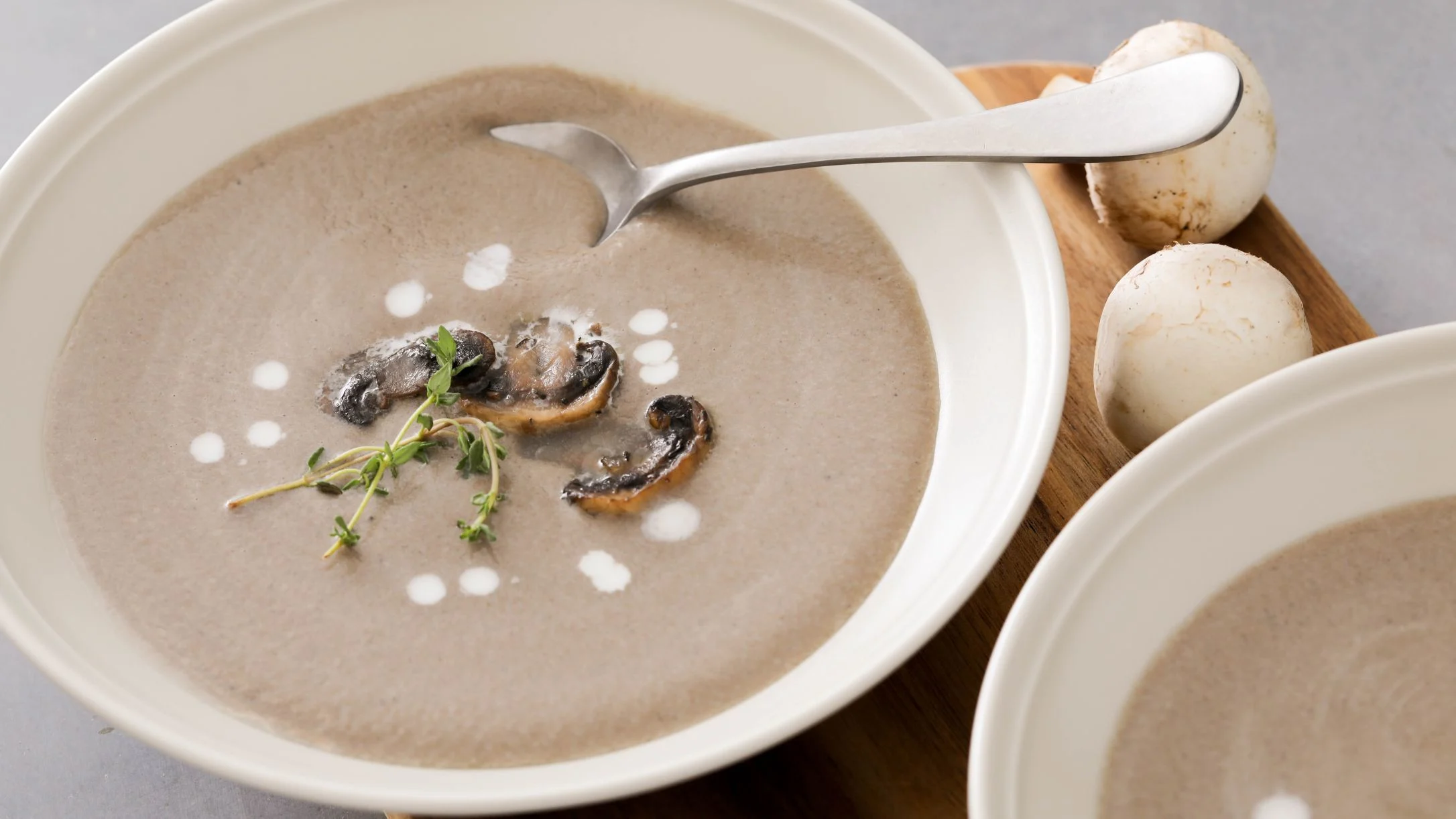 Creamy mushroom soup in white bowl with fresh mushroom slices, herb garnish, and cream dots.