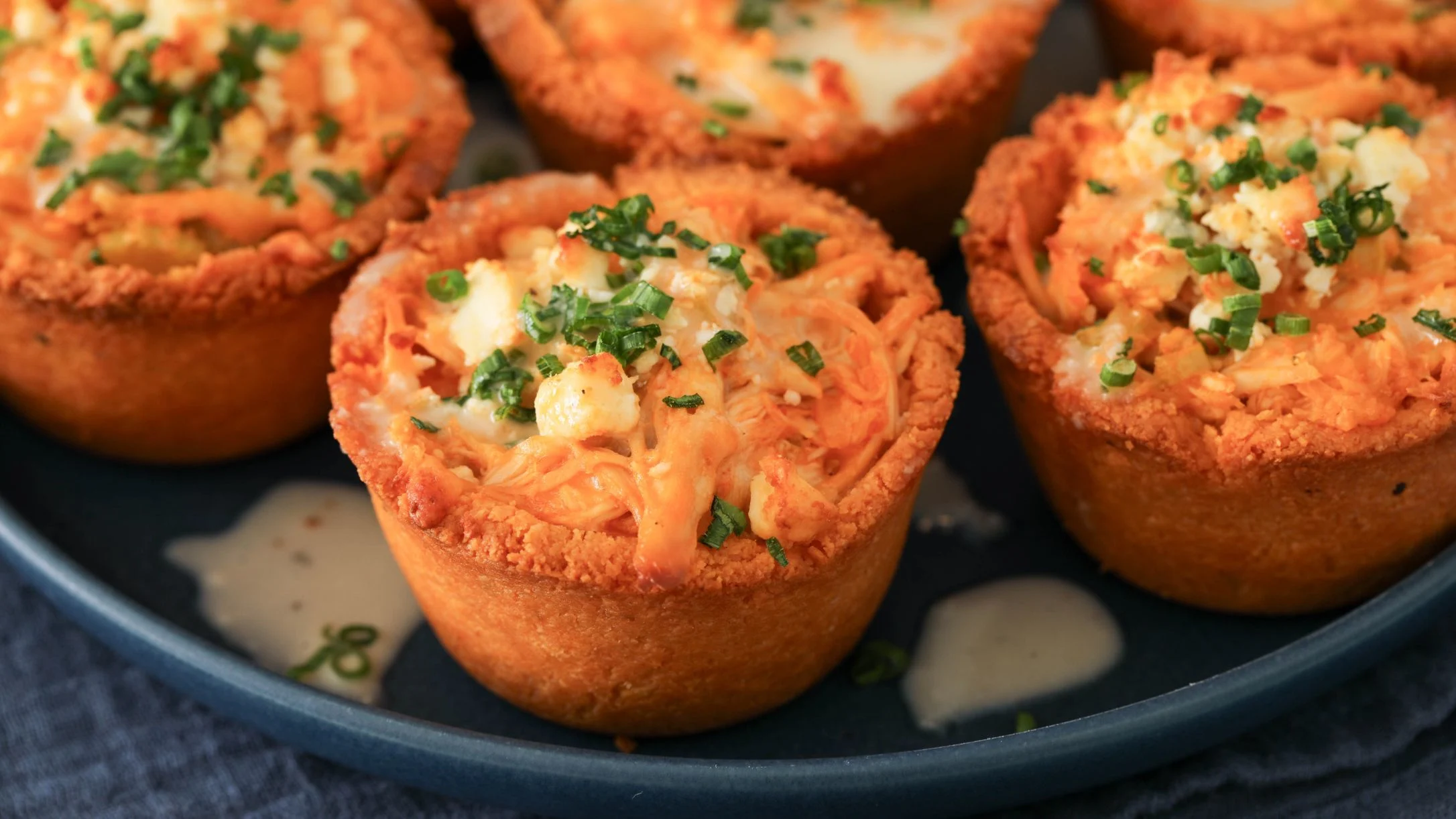 Savory mini tarts with chicken filling topped with fresh green herbs, served on a dark blue plate.