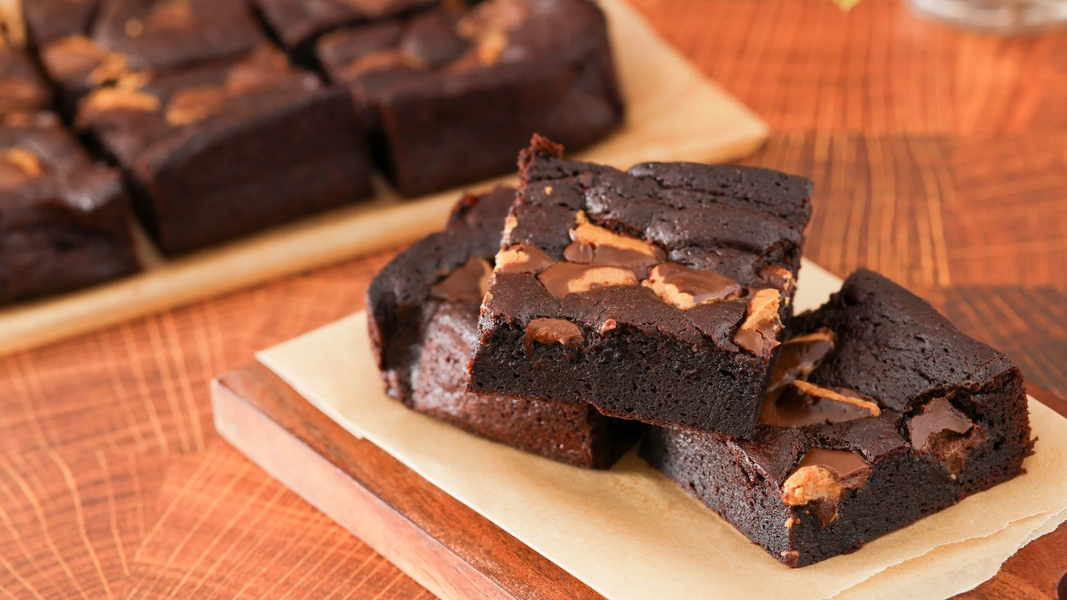 Rich chocolate brownies with peanut butter swirls stacked on parchment paper with more brownies in background.