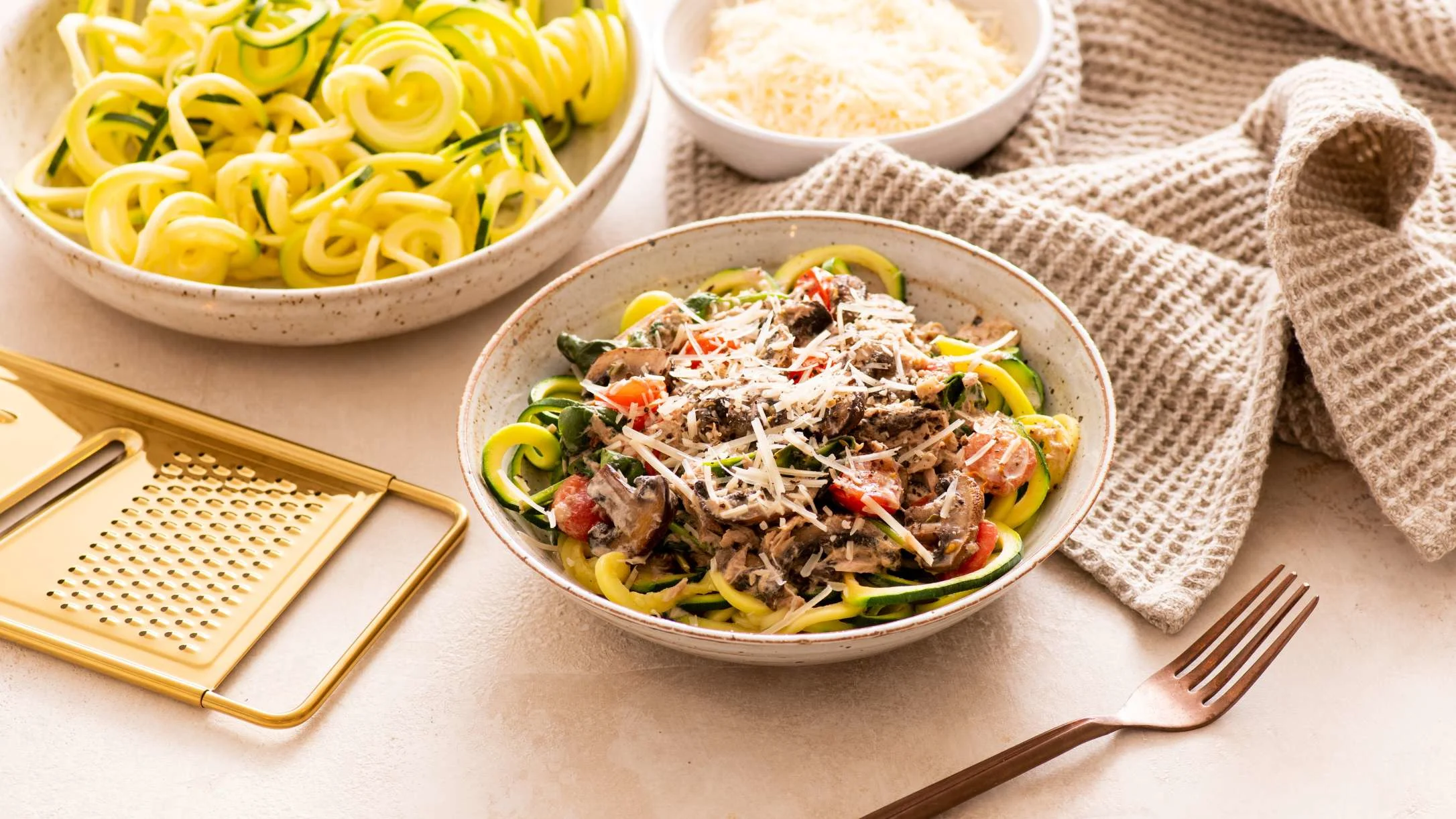 Zucchini noodle dish topped with mushrooms and cheese, served with plain zoodles and grated parmesan in ceramic bowls.