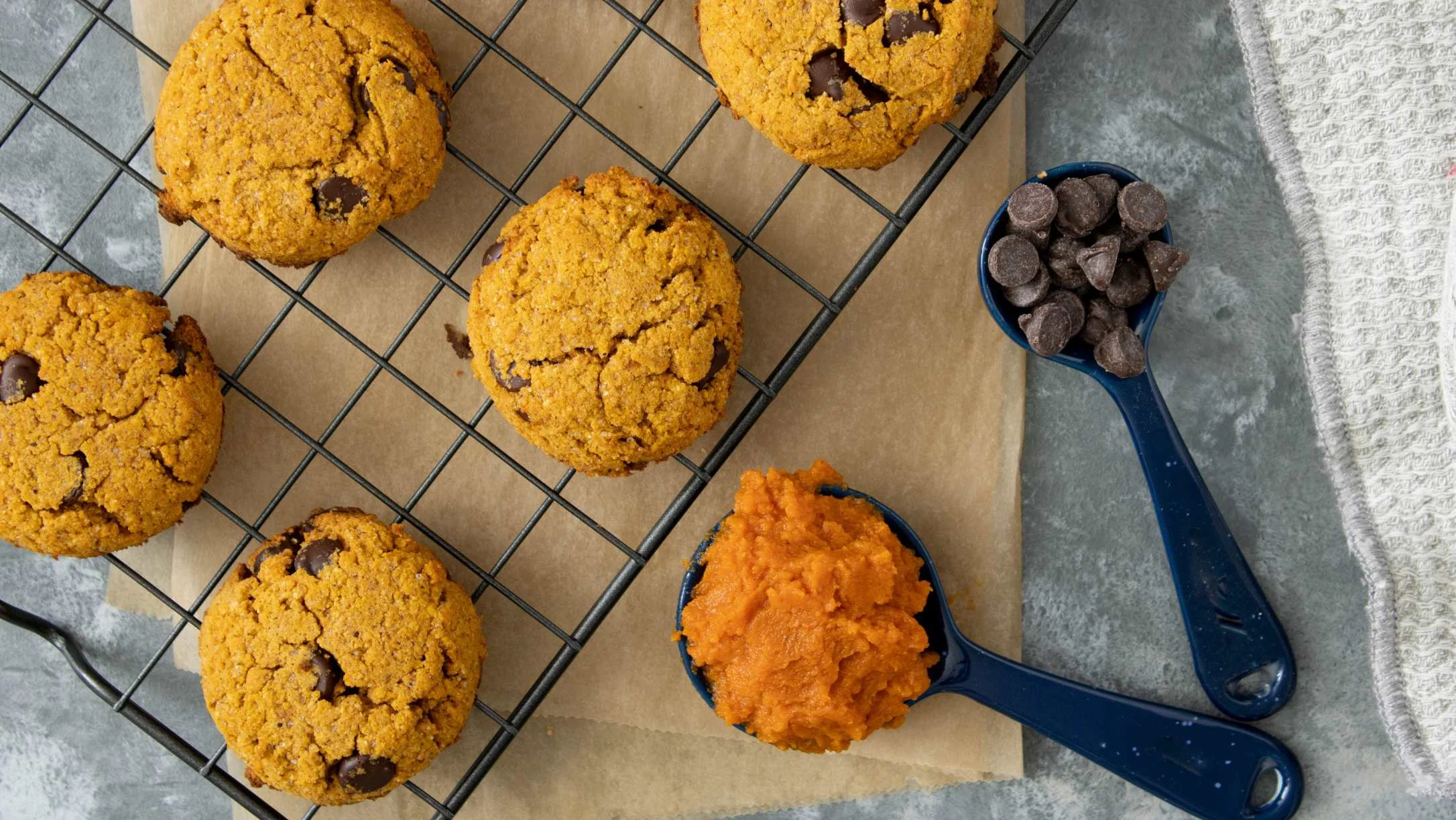 Pumpkin chocolate chip cookies cooling on a wire rack with measuring spoons of pumpkin puree and chocolate chips nearby.